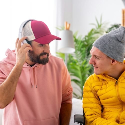 Man listening to music next to a disabled friend indoors